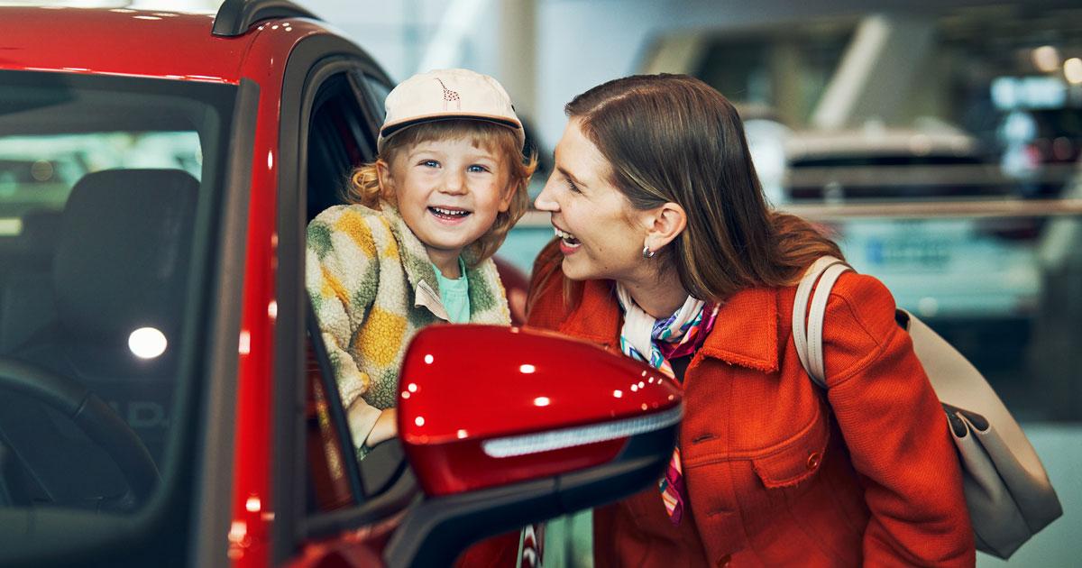 Lapsi ja aikuinen hymyilevät tutustuessaan punaiseen Volkswageniin autokaupassa